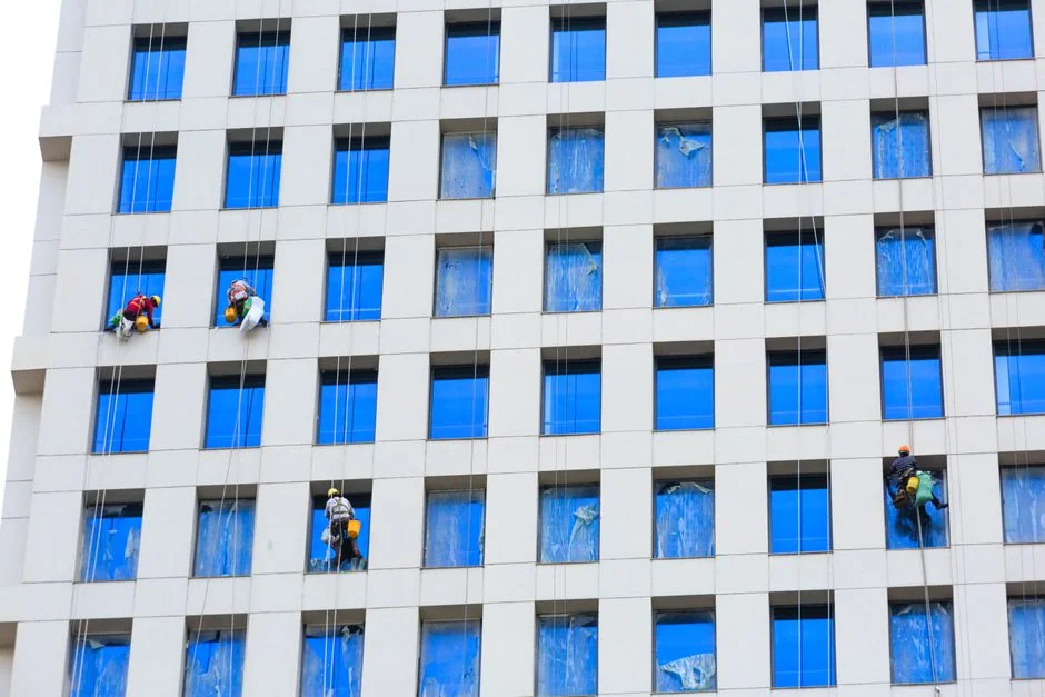 about-04 Two workers hanging to clean windows on a modern skyscraper facade.