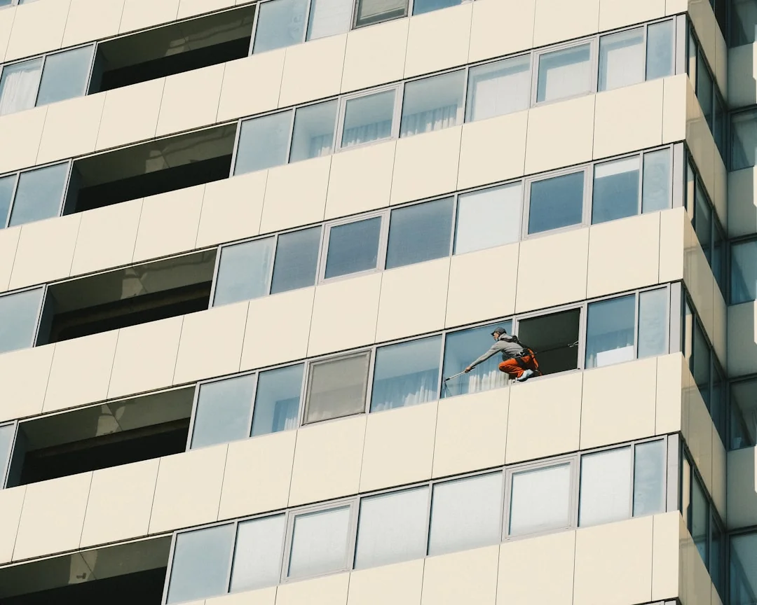Three window cleaners suspended on ropes clean a modern glass building facade during the day.